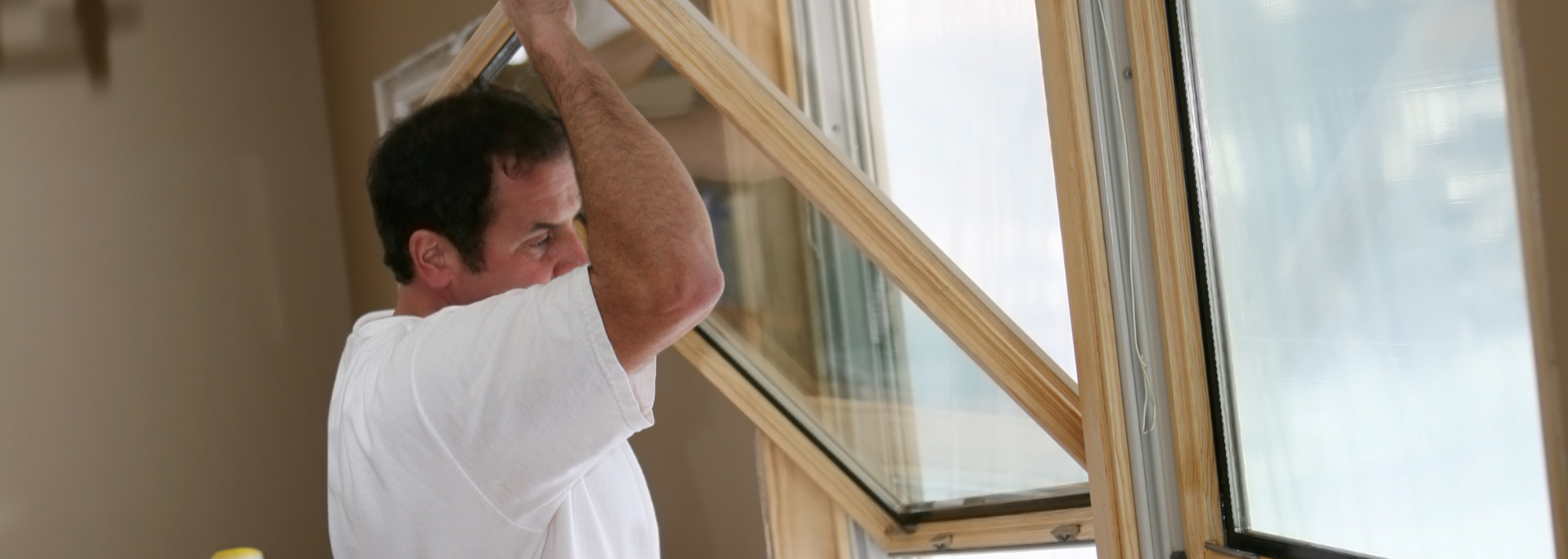 Man in a white shirt raising his arm near a sunlit window, holding a paint roller