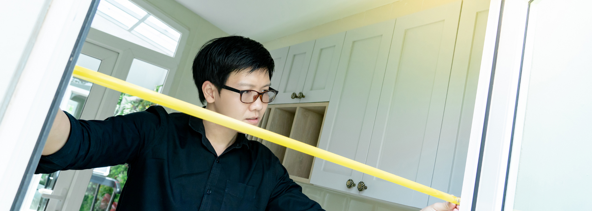 Person measuring a doorway with a yellow tape measure in a bright room