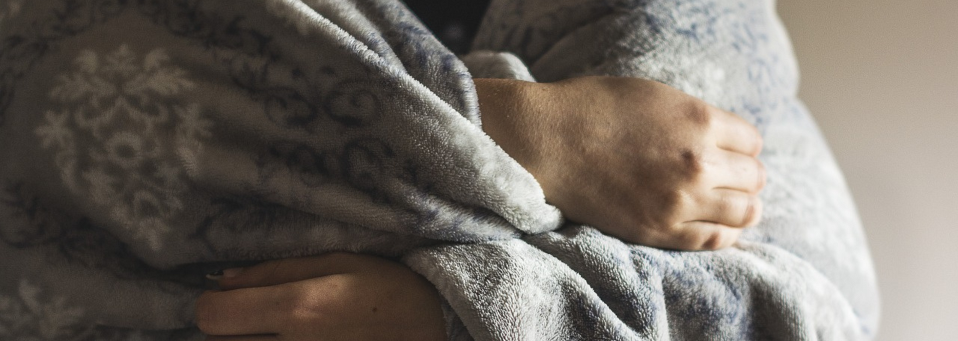 Person wrapped in a gray blanket, resting with arms crossed on a bed.