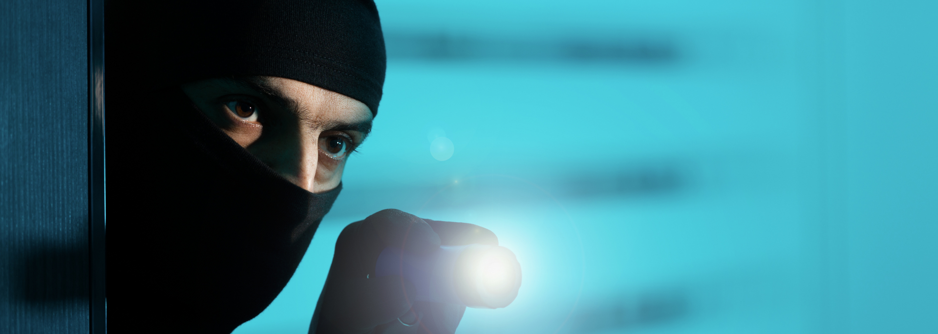 Masked person aiming a gun with a bright flashlight in a blue-lit setting