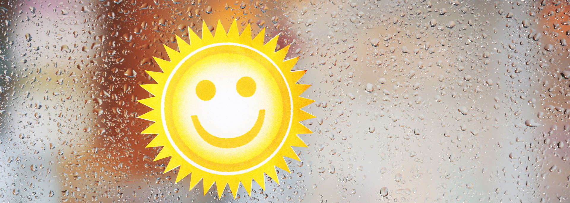 Smiling sun icon on a blurry rain-speckled window background