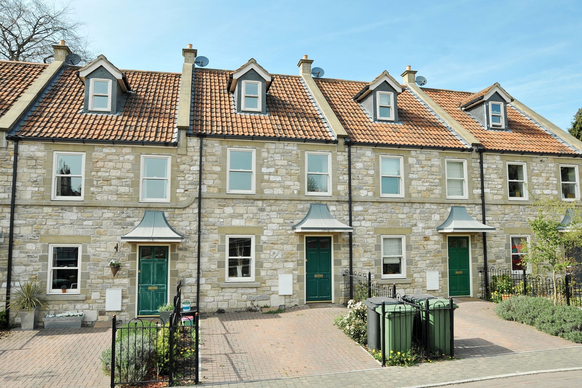 Row of stone townhouses with red-tiled roofs and green doors along a quiet street