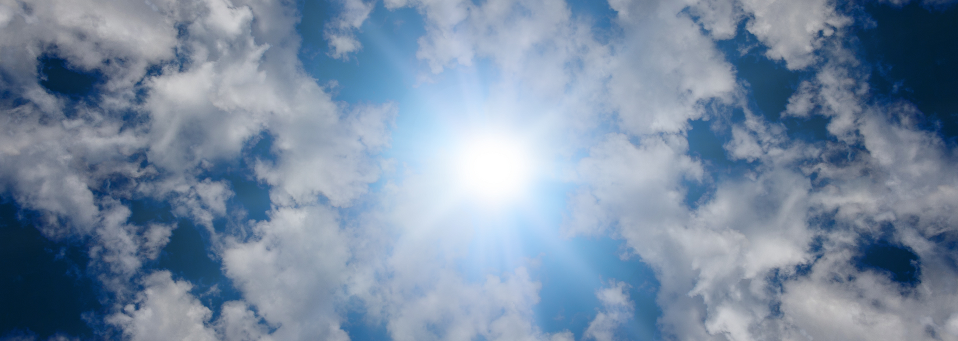 Bright sun shining through scattered clouds in a blue sky