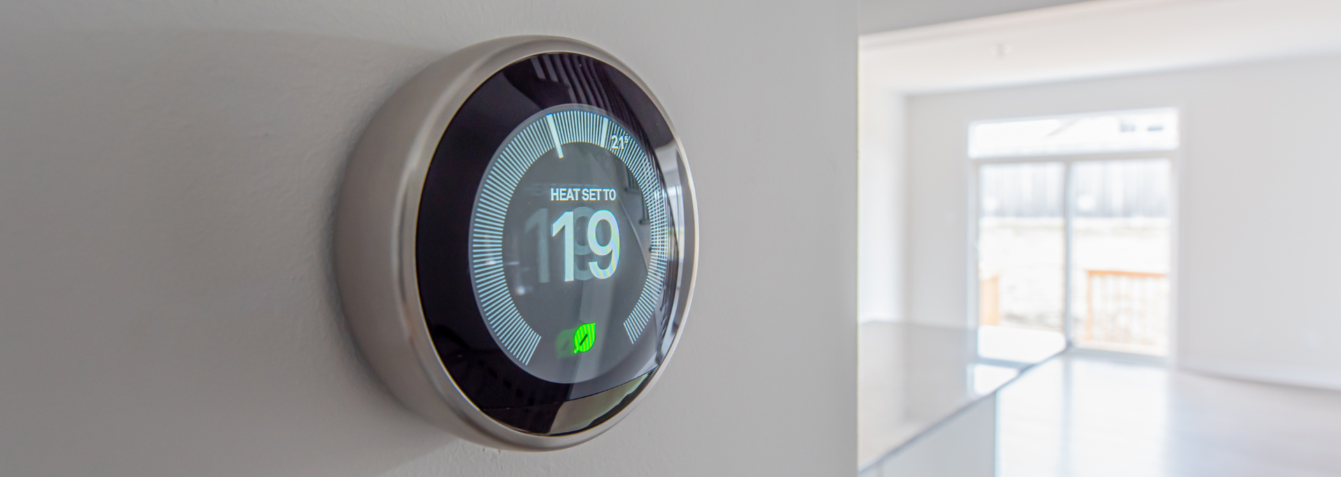 Round digital thermostat on a wall beside a bright window in a modern room