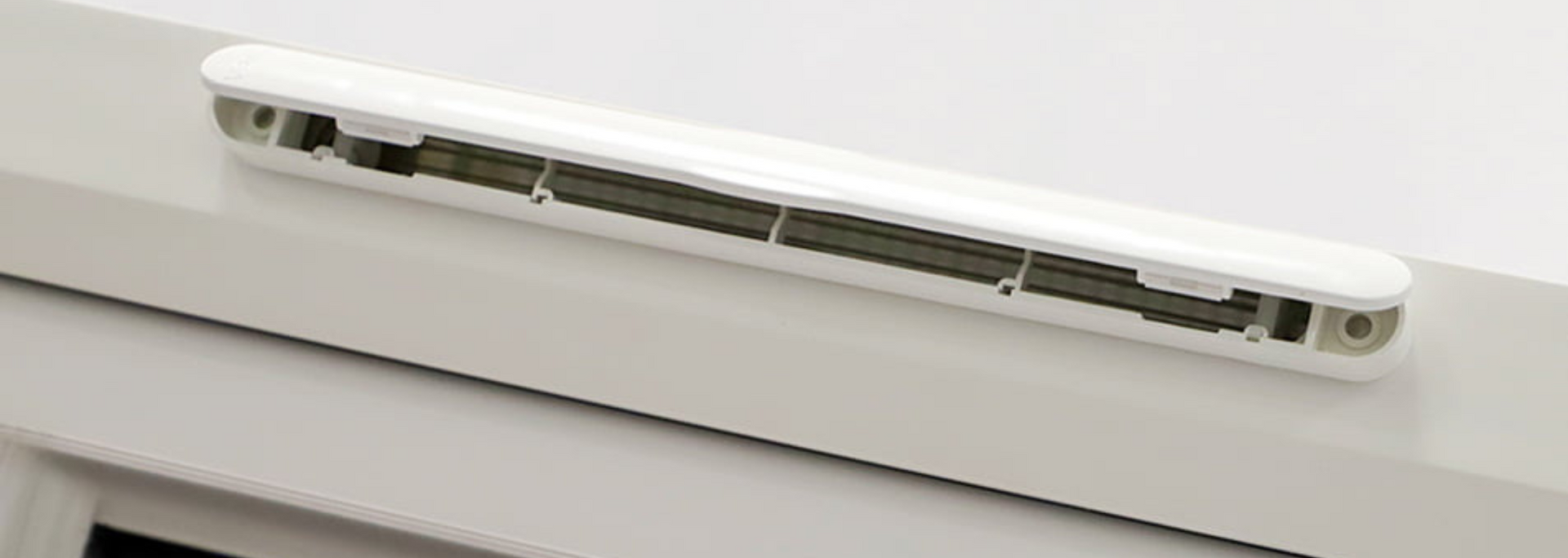 Close-up of a white wall-mounted air vent with a dark interior slot on a light ceiling