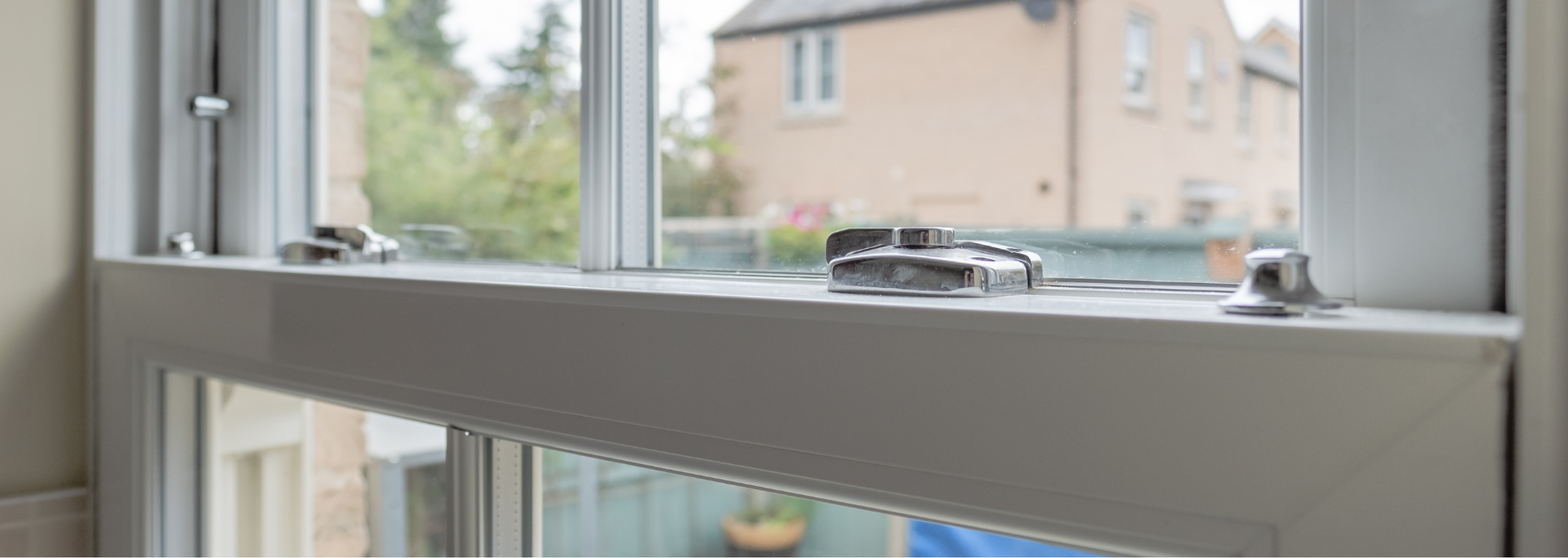 Close-up of a white window frame with a silver latch, overlooking a suburban house outside