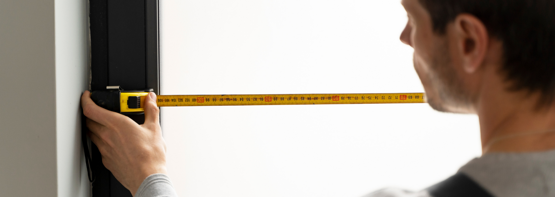 Person measuring a wall with a tape measure, marking the edge with a pencil.
