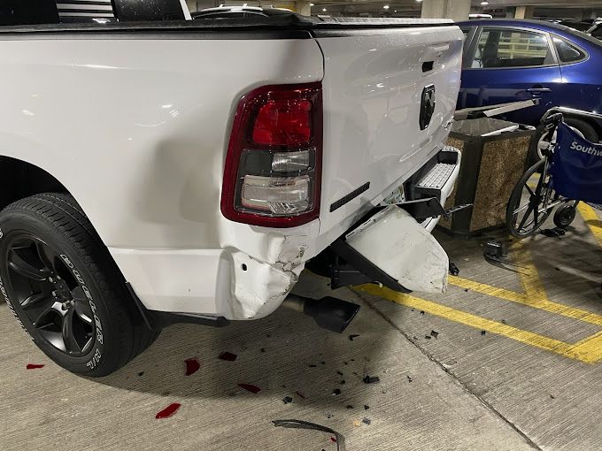 A white truck with a damaged bumper is parked in a parking lot.