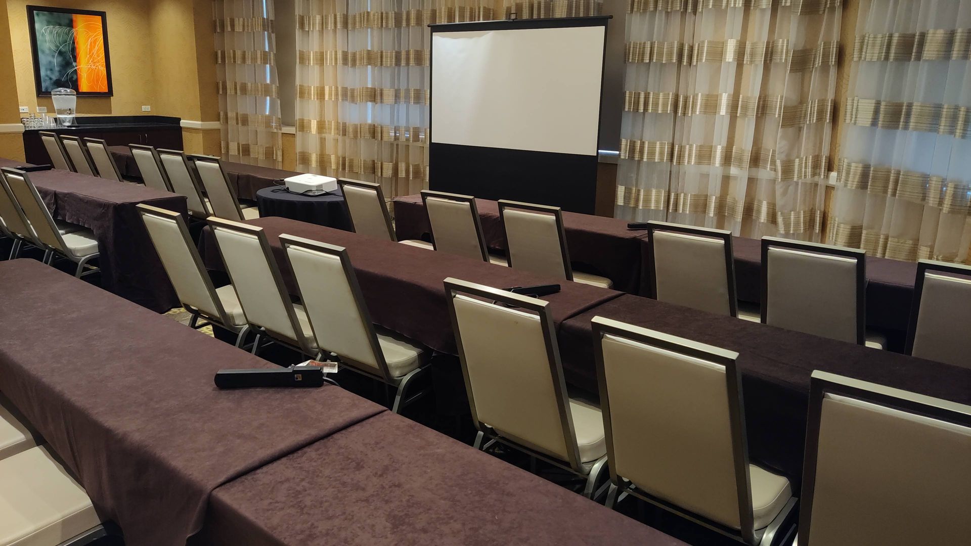 A conference room with tables and chairs and a projector screen