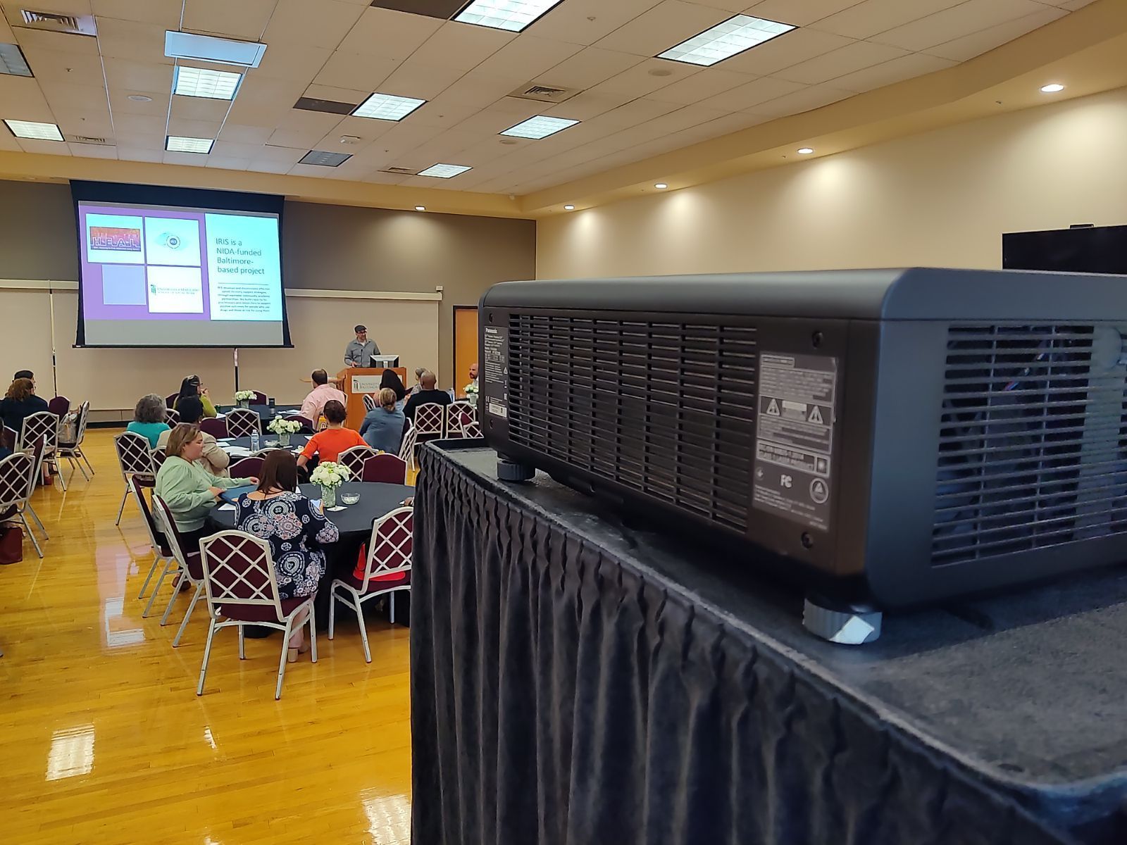 A large room with tables and chairs and a projector screen.