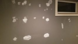 Gray wall with multiple patches of white compound; a small window is in the top right.