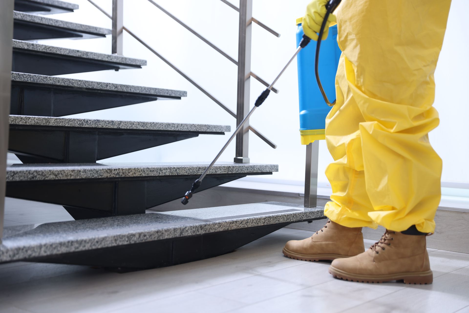 Person in yellow protective suit spraying disinfectant on stairs with a blue backpack sprayer
