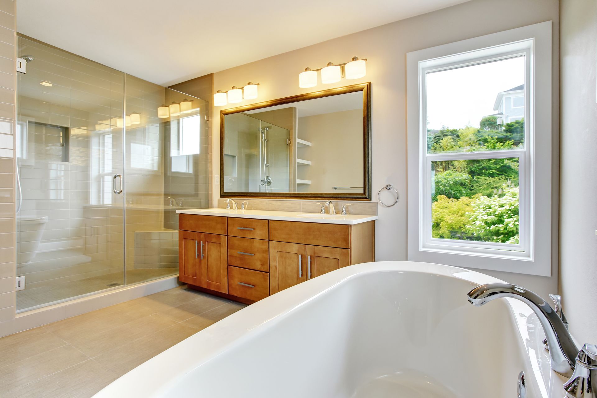 Modern bathroom with glass shower, wood vanity, large mirror, and a white bathtub by a window.