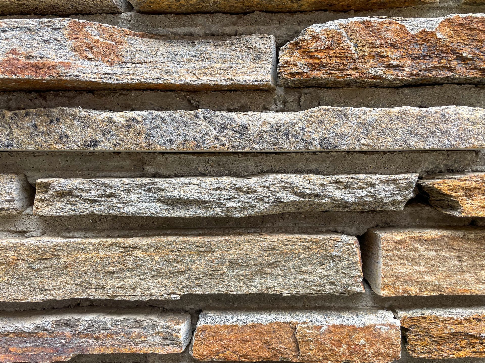 Close-up of a stacked stone wall with gray, tan, and rusty orange layers.