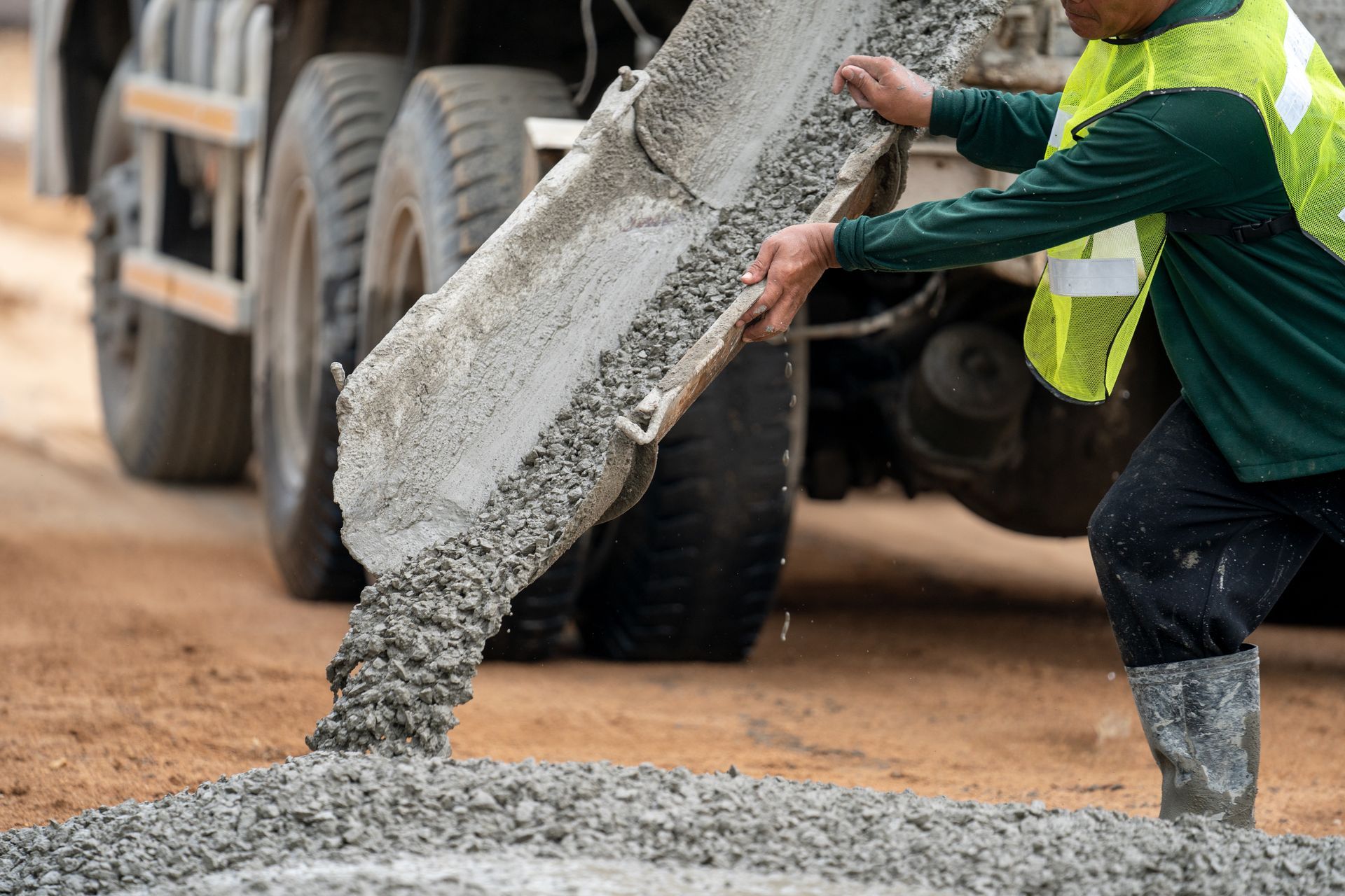 Worker in a neon vest pouring wet concrete from a truck onto a road surface