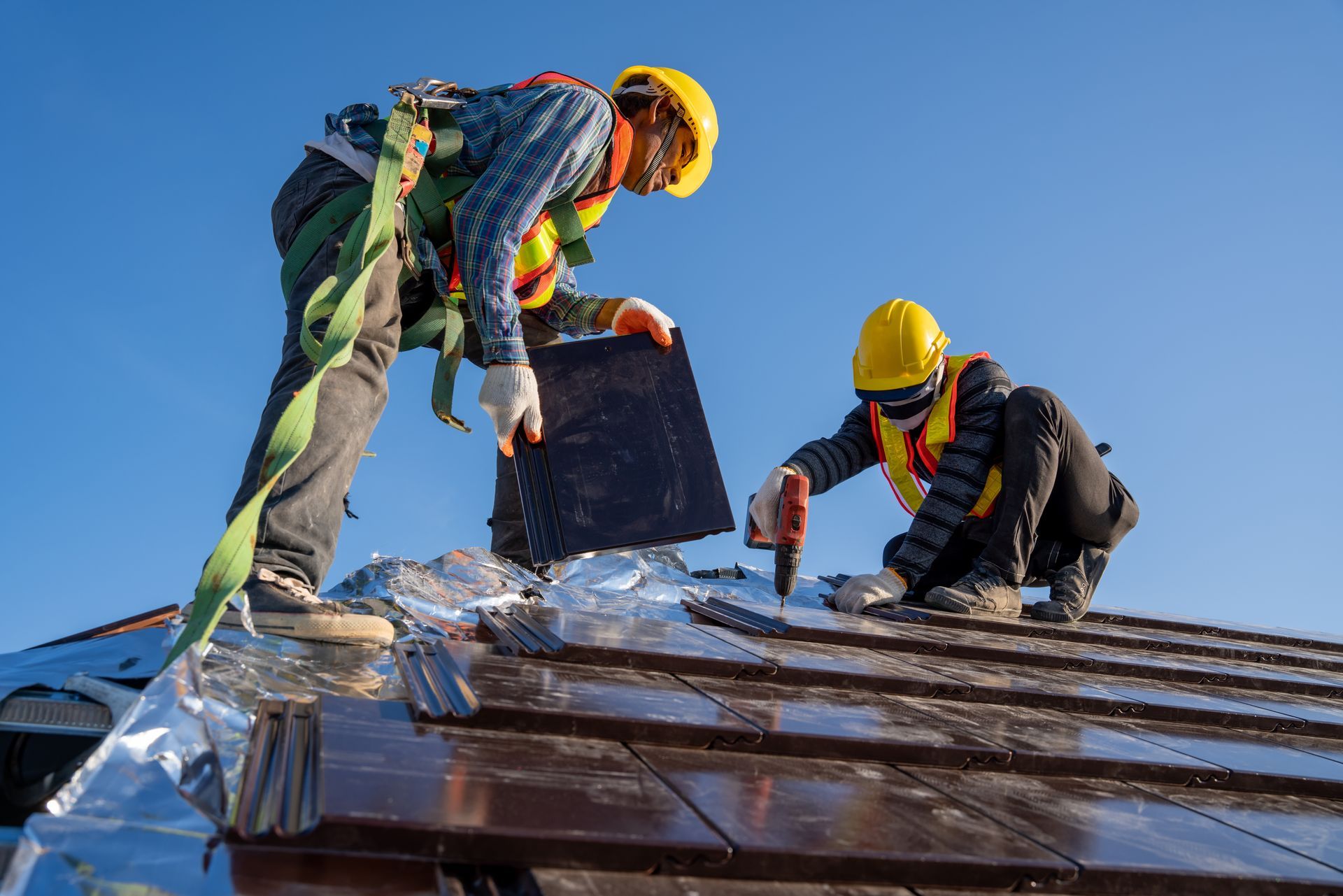 Two workers in hard hats repairing a roof under a blue sky