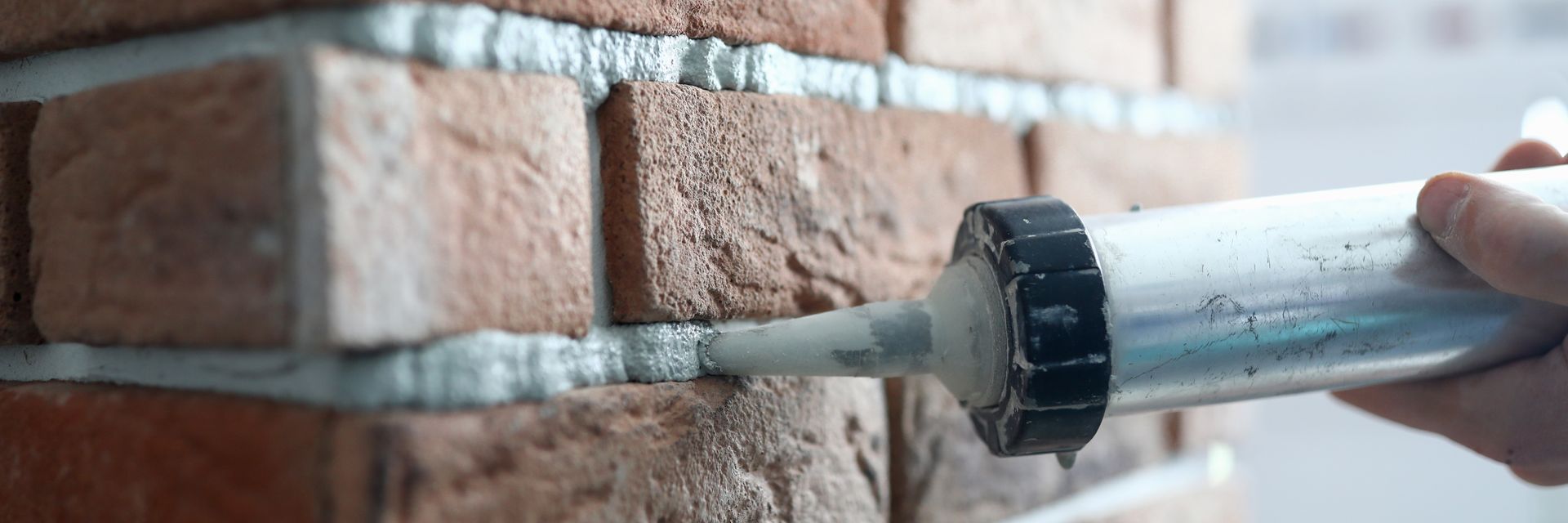 Caulking gun applying sealant along a brick wall seam with visible gaps