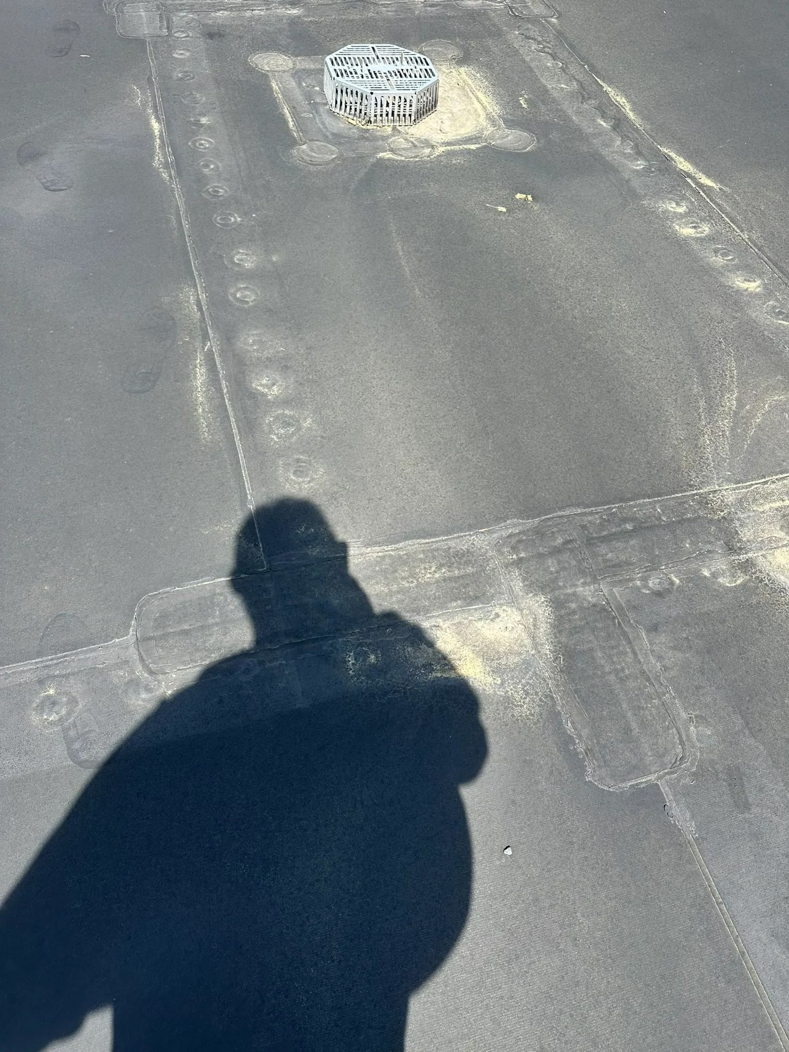 Shadow on sunlit pavement near a small drain or vent cover