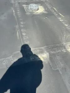 Shadow of a person on a rooftop beside a small vent on a gray surface