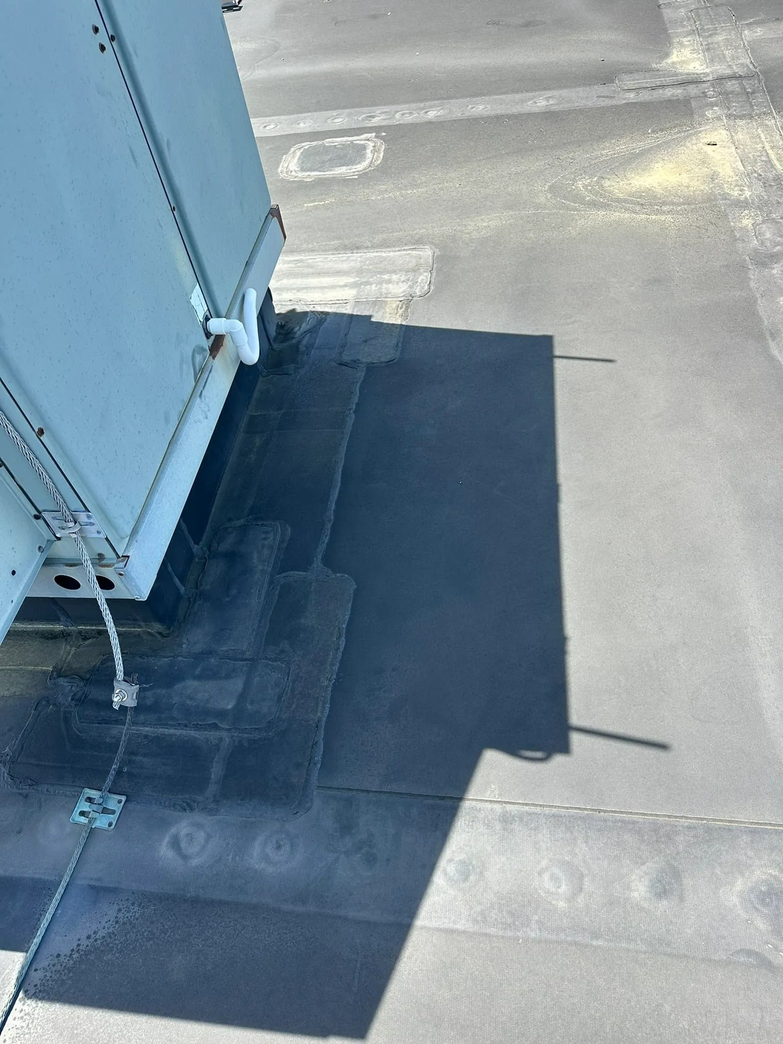 Flat rooftop with a large dark rectangular patch beside a light gray metal structure and shadow.