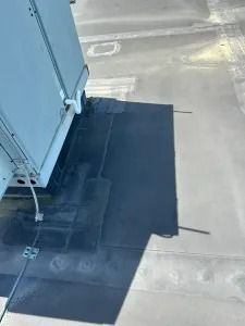 Rooftop view of a building corner with a dark rectangular patch on the surface and a small antenna.
