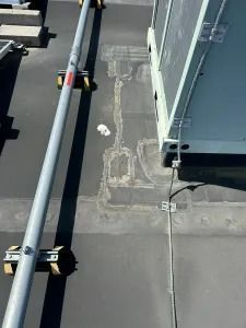 Rooftop HVAC unit beside a cable and patched concrete surface near a metal railing.