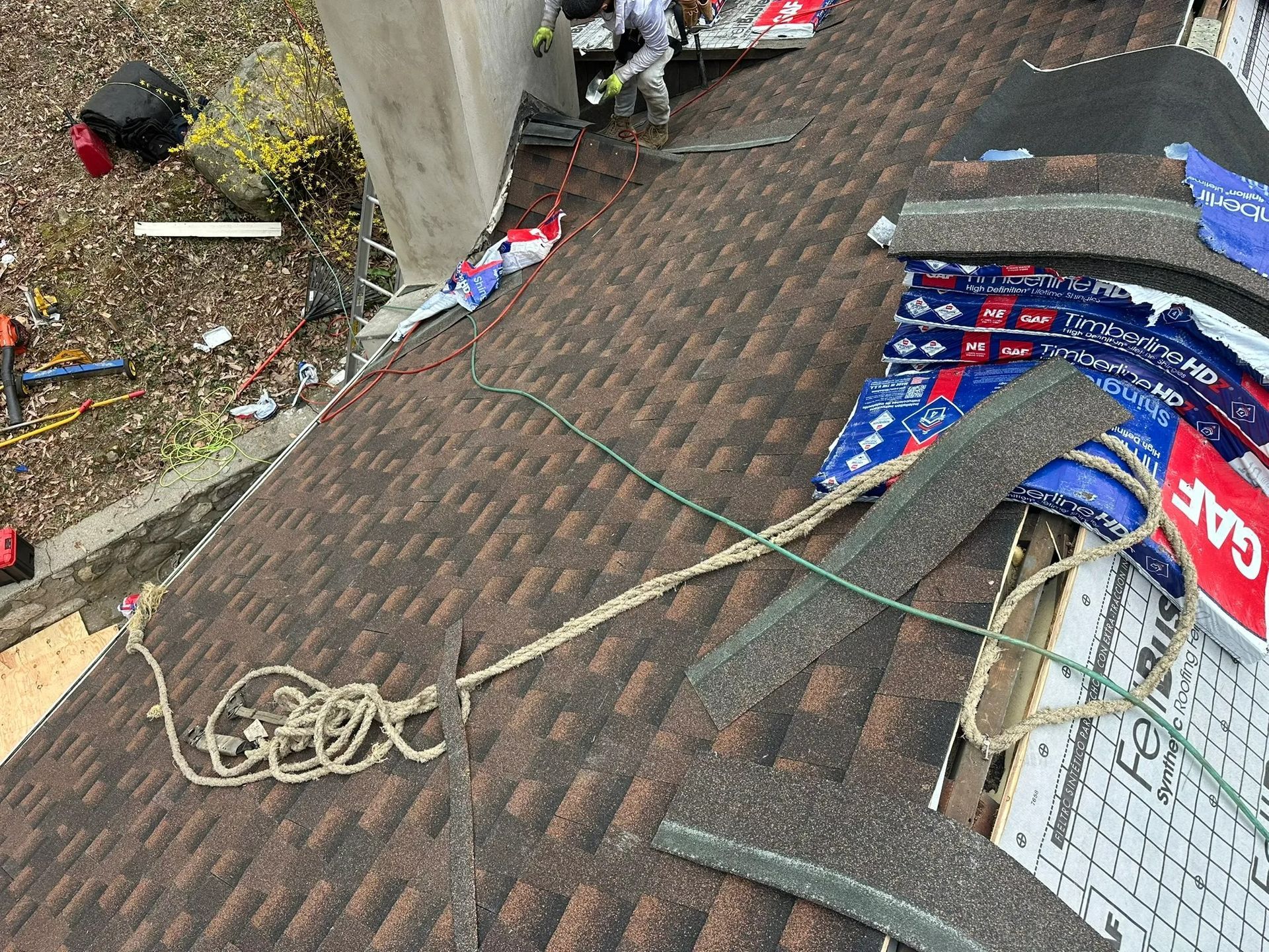 Roof with tangled wires and debris beside a wall, including a blue tarp and broken materials