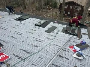 Workers installing roofing underlayment on a steep roof in a wooded area