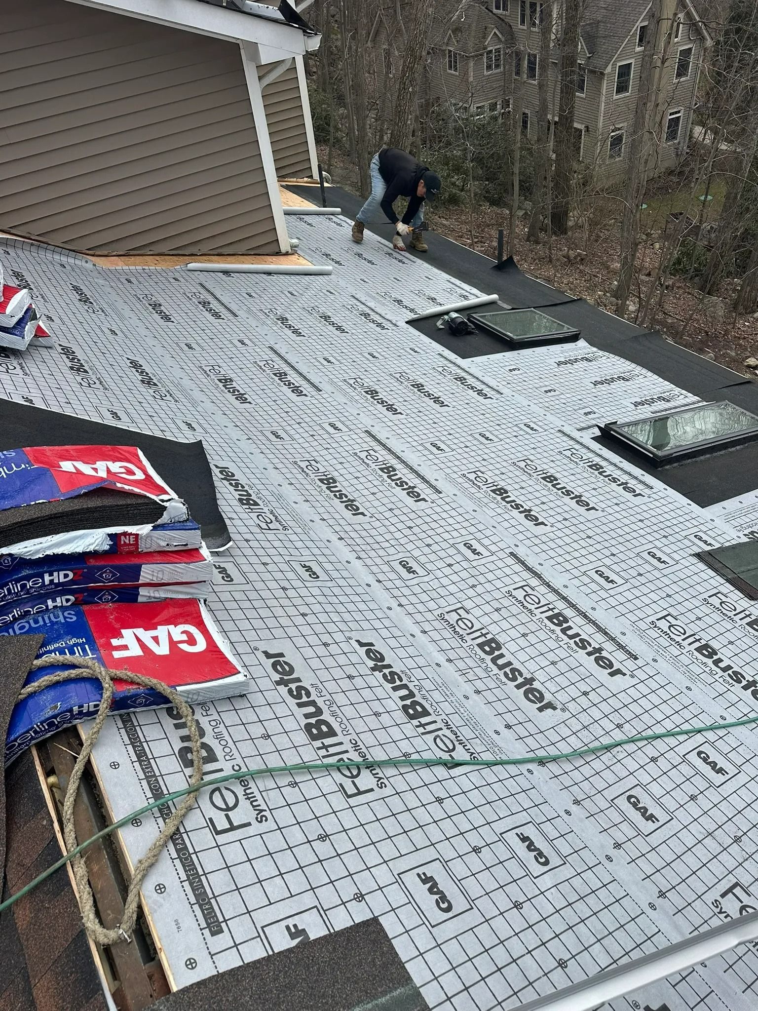 Roof under repair with white underlayment, scattered shingles, and a worker near the ridge line
