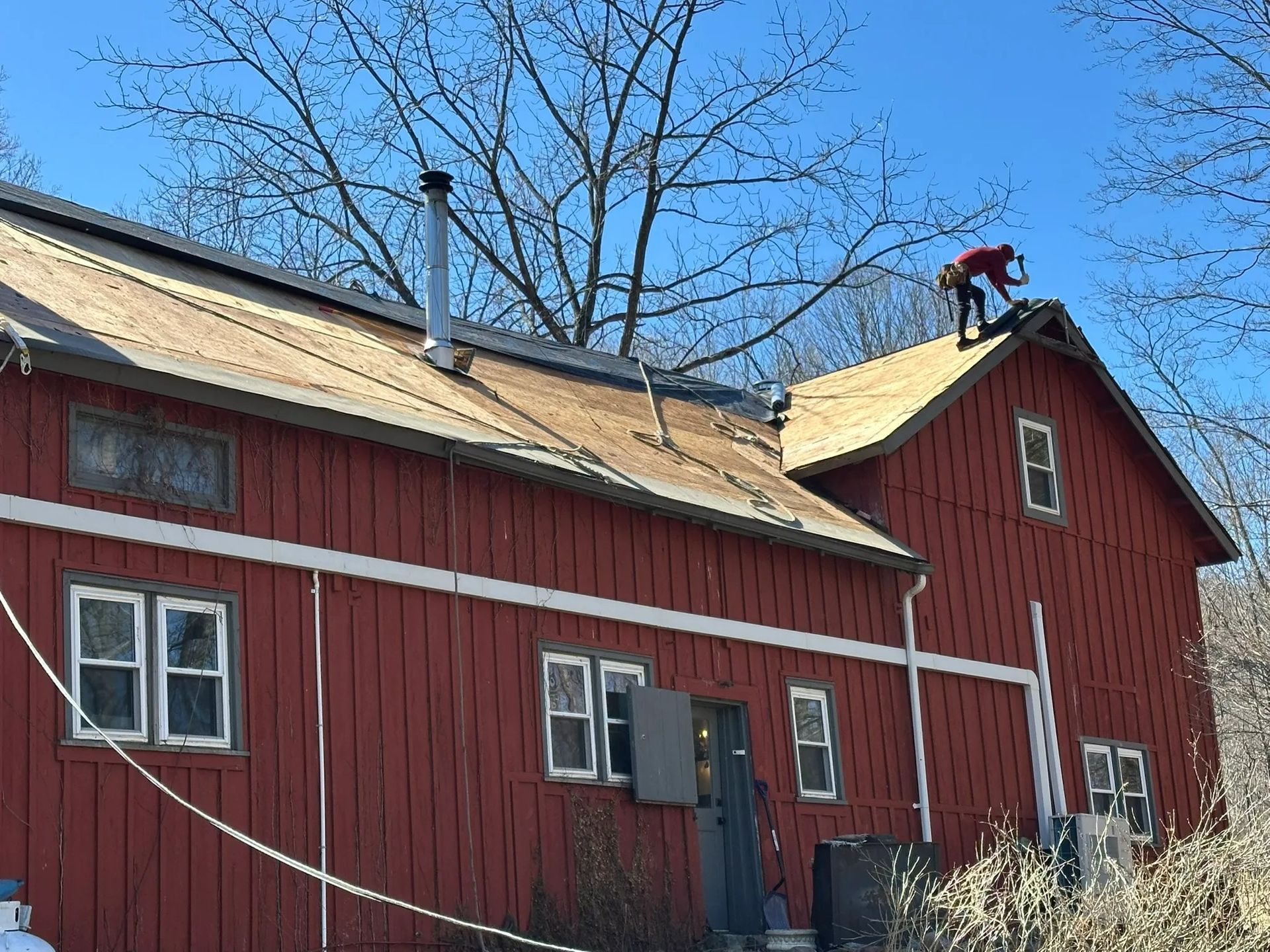 Red barn with white trim and rooftop chimney under a clear blue sky, with bare trees behind it