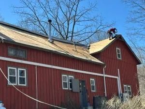 Red barn with white trim and a person on the roof under a blue sky