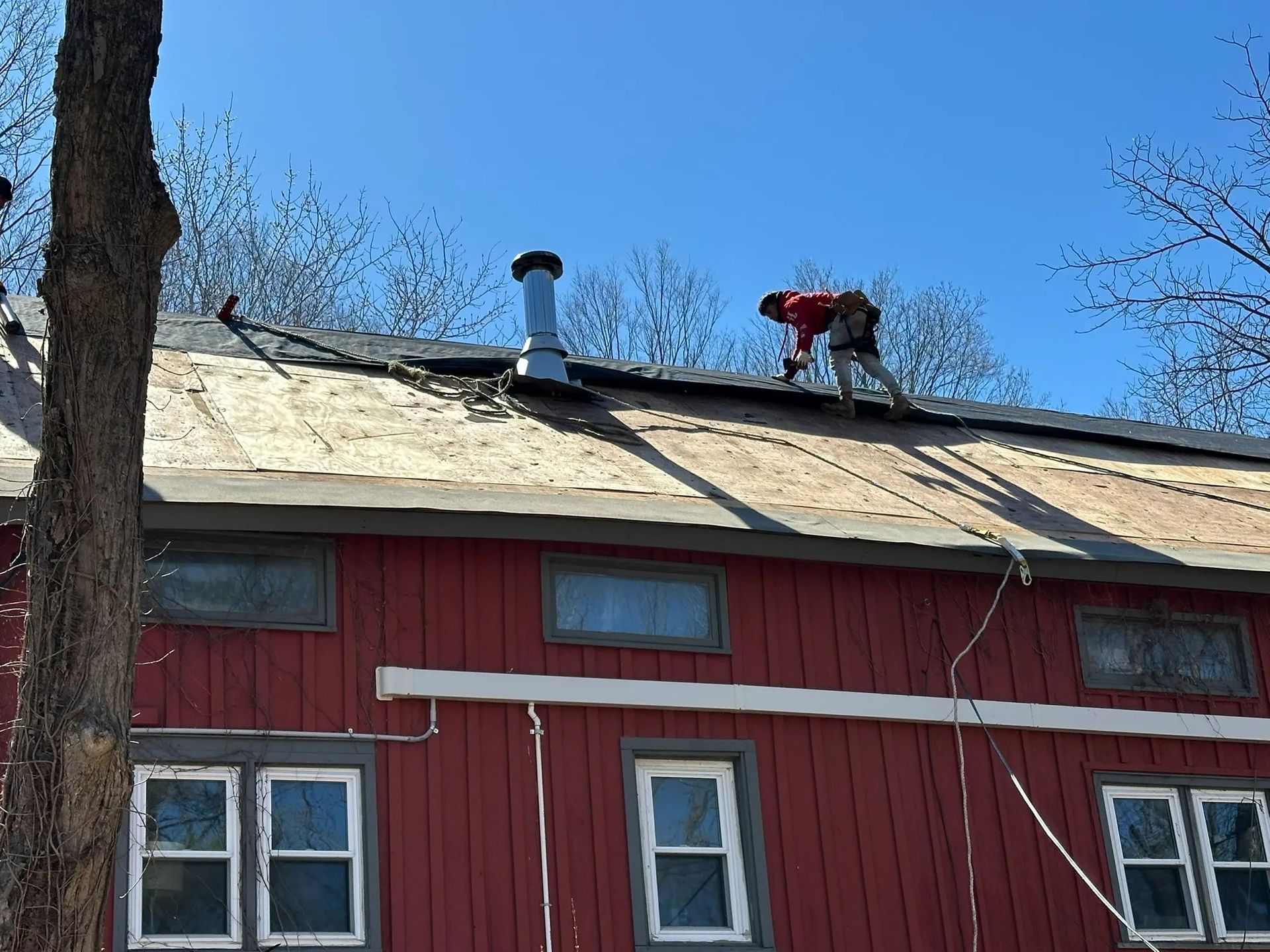 Person on roof repairing red barn roof under blue sky