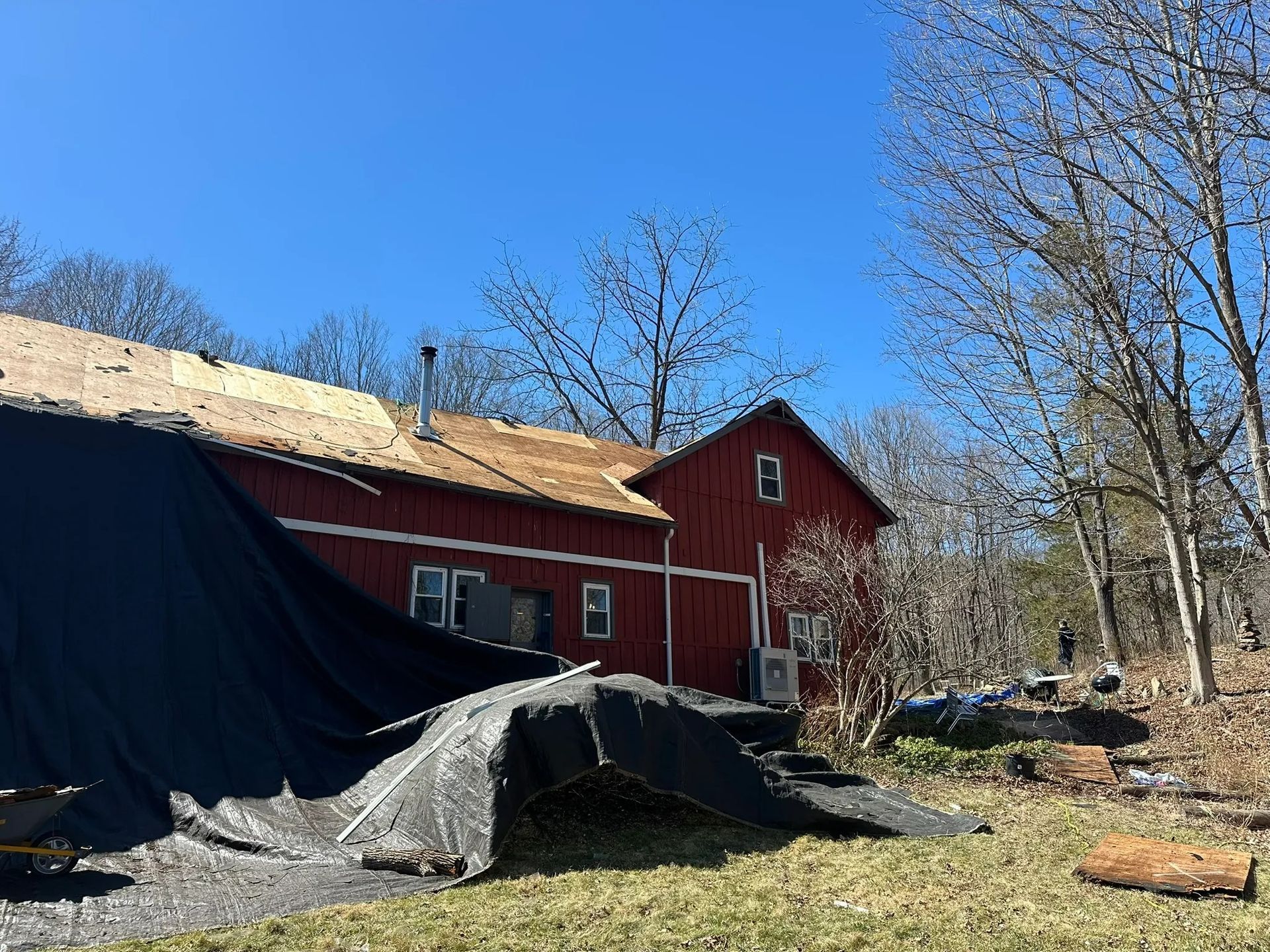 Red barn beside a tarp-covered pile of gravel under a clear blue sky, with leafless trees nearby