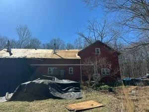 Red barn with tarped equipment in a yard beside leafless trees under a clear blue sky