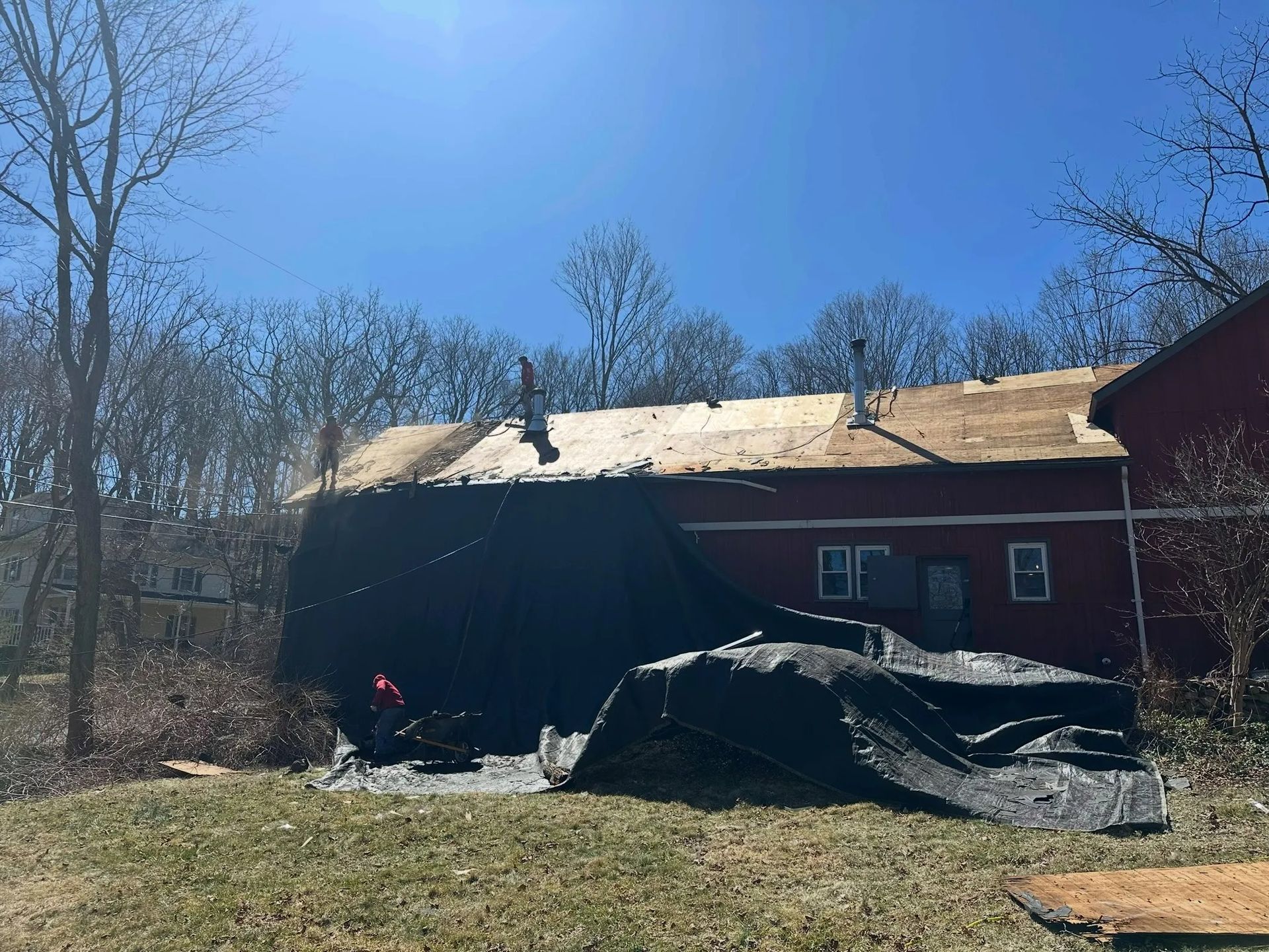 Red house with a collapsed dark roof in a wooded yard on a sunny day