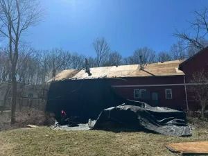 Damaged red building with collapsed roof and tarp-covered debris in a wooded area