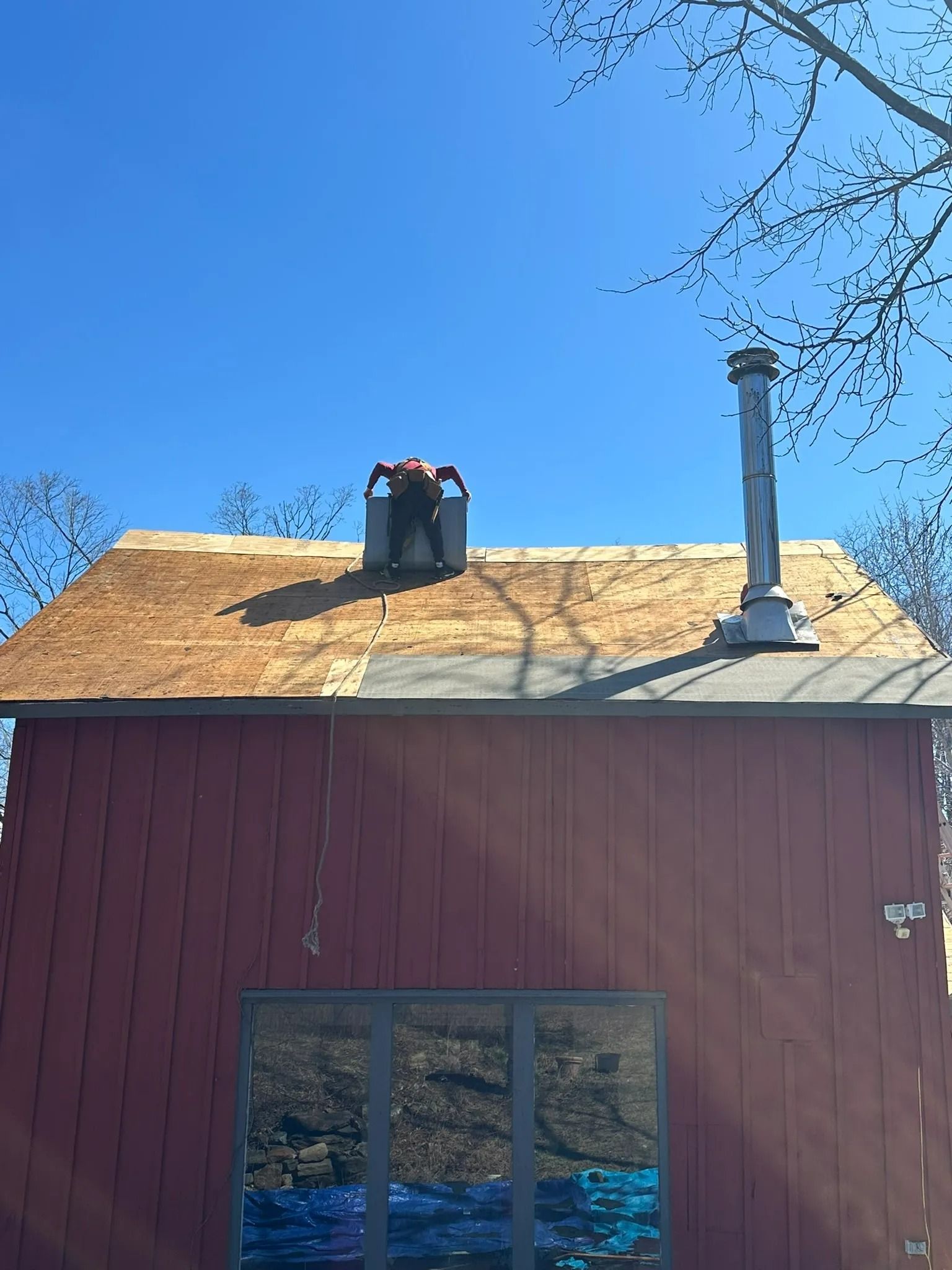 Red barn with tan roof, black chimney, and white vent pipe against a clear blue sky.
