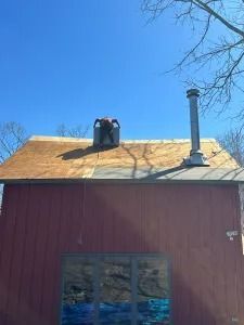 Red barn roof with two chimney vents under a clear blue sky