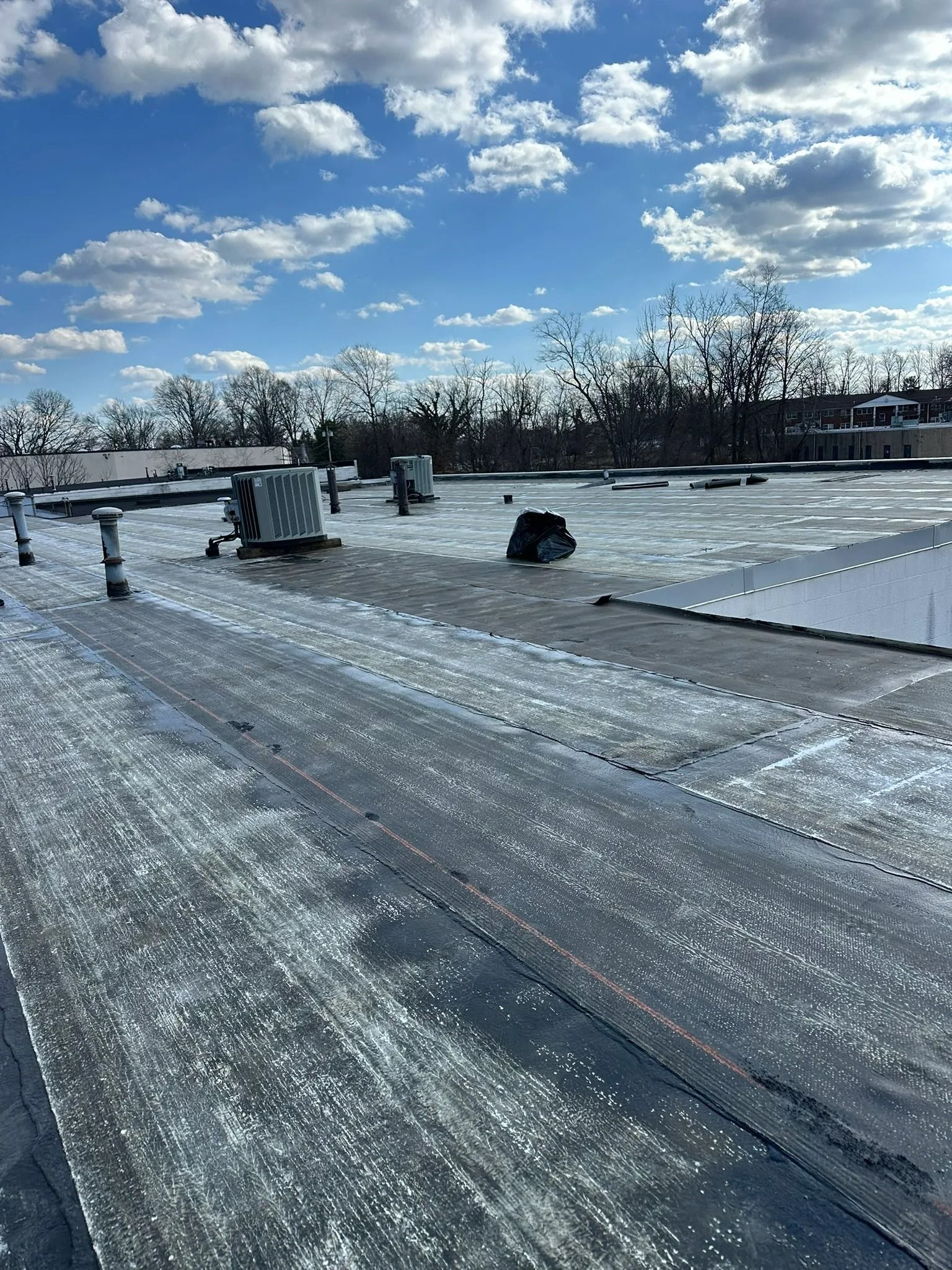 Snow-covered rooftop with scattered equipment under a bright blue sky and clouds