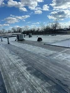 Flat rooftop under a blue sky with clouds, showing vents and a low parapet wall.