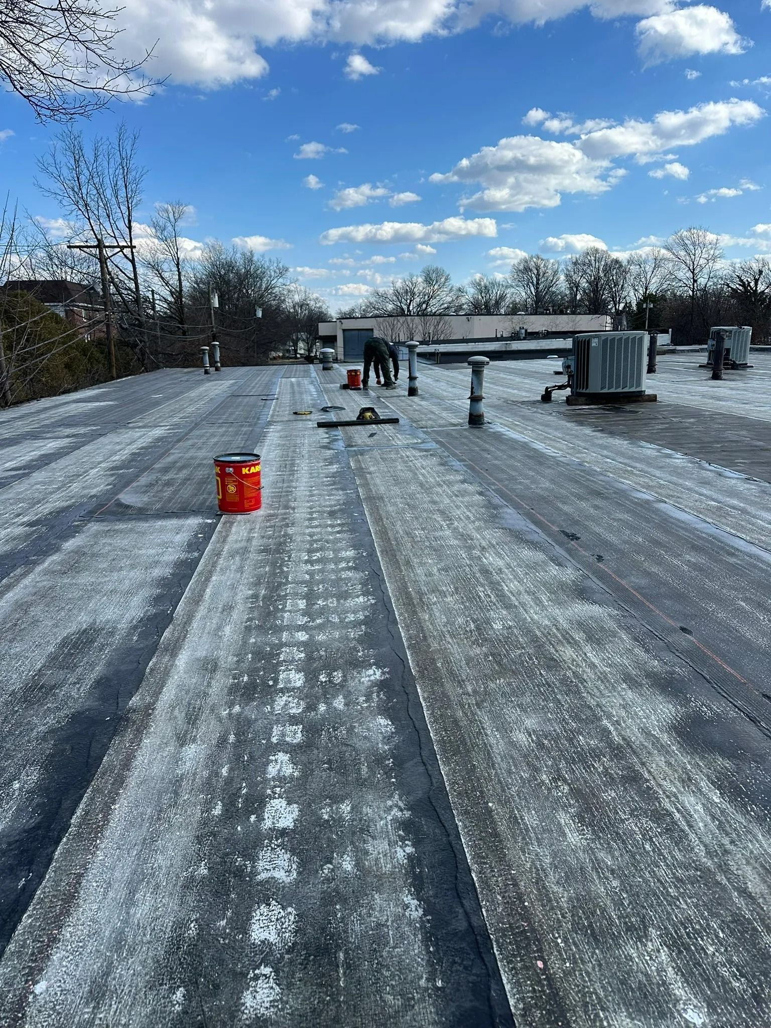 Snow-dusted rooftop with a small red bucket, HVAC units, and a bright blue sky with clouds.