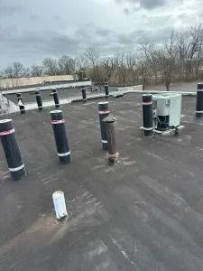 Rooftop with black vent pipes, HVAC units, and bare trees under an overcast sky