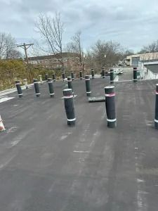 Outdoor rooftop with evenly spaced black bollards and a few cones on a flat surface, under a cloudy sky