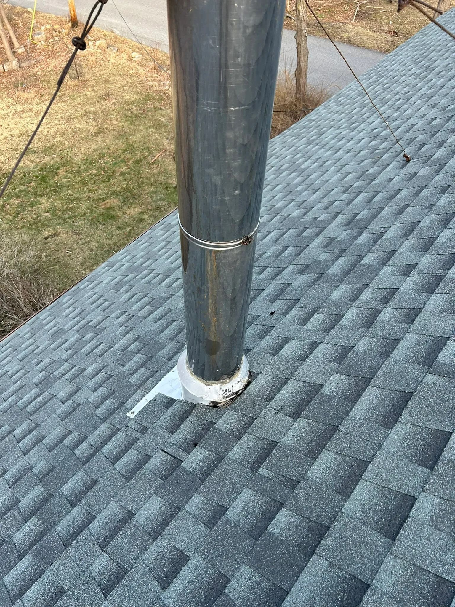 Metal vent pipe protruding through a gray shingled roof, sealed with white flashing trim