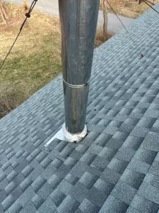 Metal chimney pipe through gray shingle roof with flashing and guy wire support