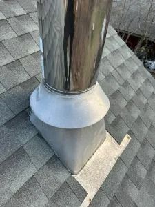 Metal chimney pipe with flashing on a gray shingled roof