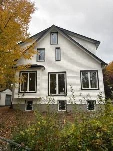 White two-story house with gray roof and autumn foliage in front yard