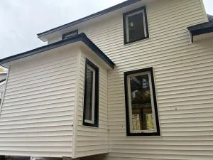 White house exterior with beige siding and black-trimmed windows against a cloudy sky