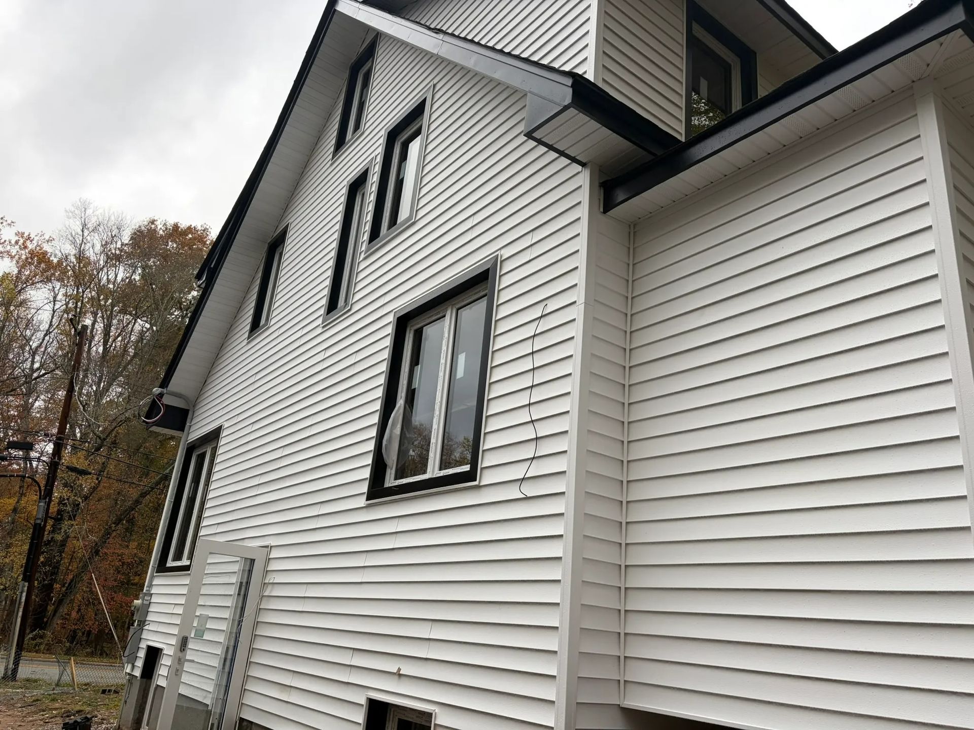 White vinyl-sided house exterior with black-trimmed windows and a sloped roof, viewed from the side
