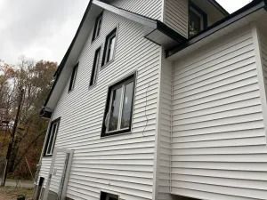Side view of a white vinyl-sided house with black-trimmed windows and a sloped roof.